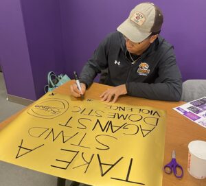 Volunteer prepares to take part in a Community Outreach Event for Domestic Violence Awareness Month. The sign reads "Take a Stand Against Domestic Violence" and also features the word silence with a cancel sign over it.